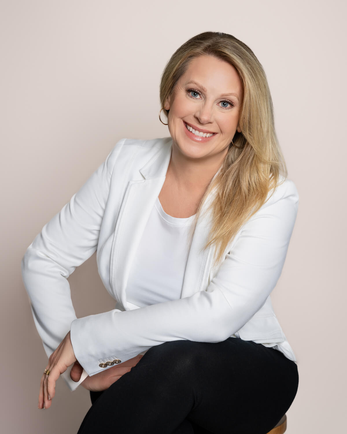Julie Hood, online business manager, smiling in a white blazer and black pants during a professional studio portrait.